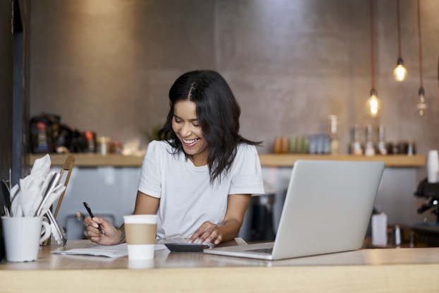  Smiling woman working at a laptop inside her shop.