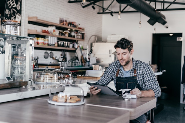 Business owner going over receipts with a tablet inside his cafe.