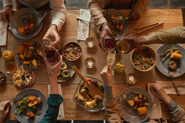 Top view of a table full of food and people's hands clinking glasses of drinks.