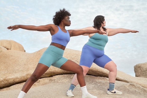  Two people doing yoga poses outdoors while wearing Girlfriend Collective exercise clothing.