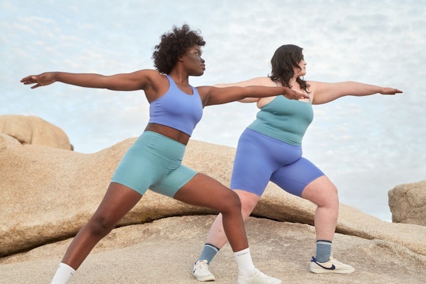 Two models doing yoga outdoors wearing pastel-colored Girlfriend Collective activewear.
