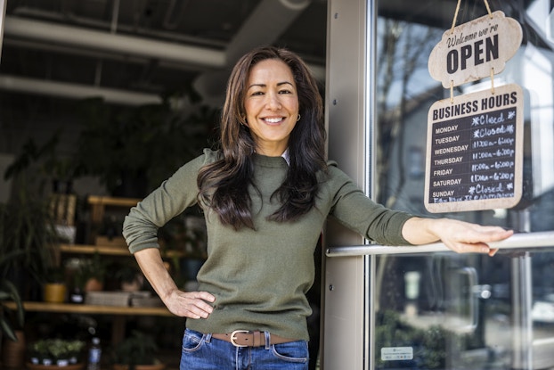  Smiling woman business owner standing in front of her business open sign.