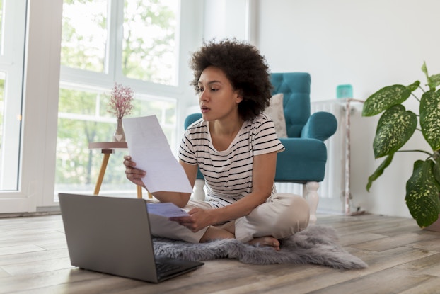  Woman looking over paperwork while working on laptop at home.