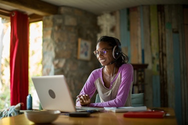  Woman sitting in her home office working on her laptop and wearing headphones. 