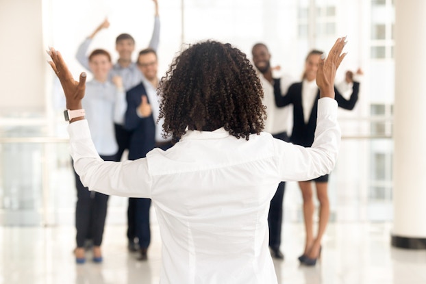 The back of a business leader motivating a team of happy employees.