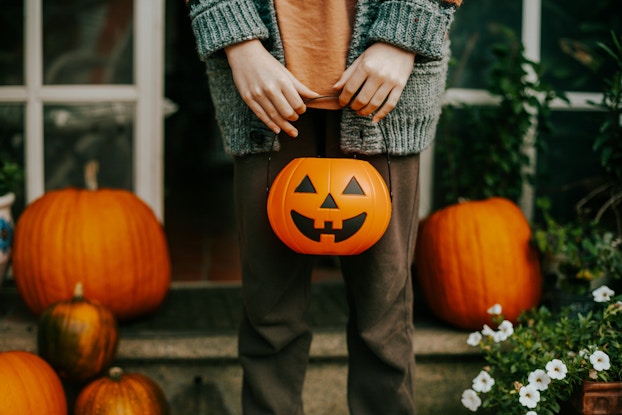 Boy's hands holding a pumpkin Halloween basket with pumpkins in the background.
