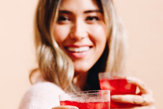 Woman holding heywell beverages in glasses.