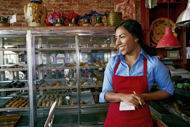  Hispanic woman wearing an apron inside a bakery.