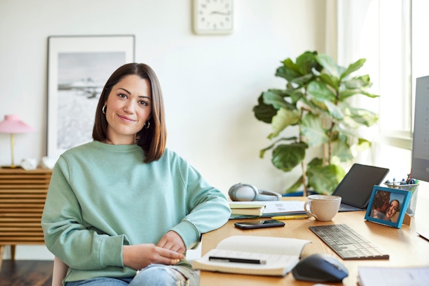  A woman entrepreneur sits in her home office. She smiles at the viewer.