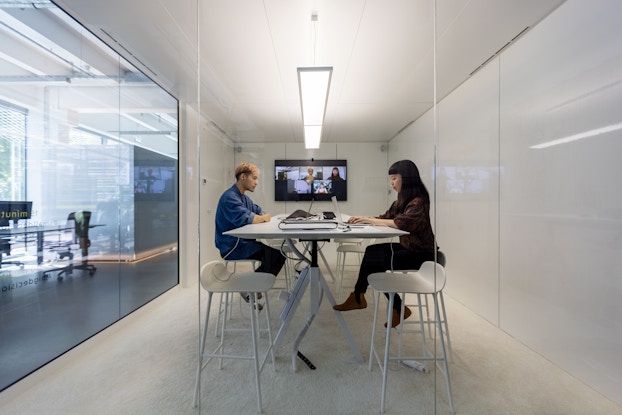 Two people in an office meeting with coworkers working remotely on video.