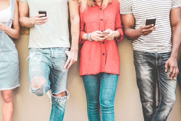 group of people leaning against a wall on smartphones