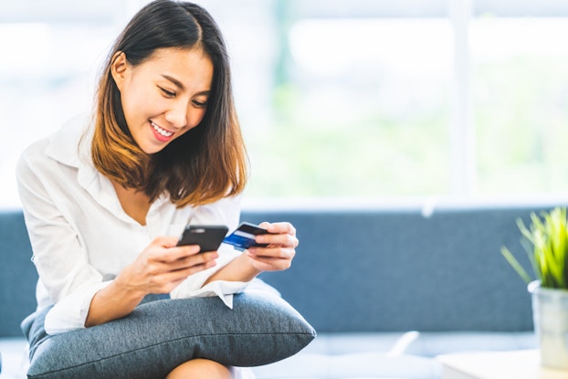  woman looking at phone holding credit card