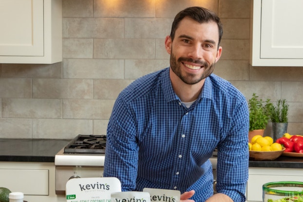 Kevin McCray, founder of Kevin's Natural Foods, in kitchen with a display of meals and seasonings.