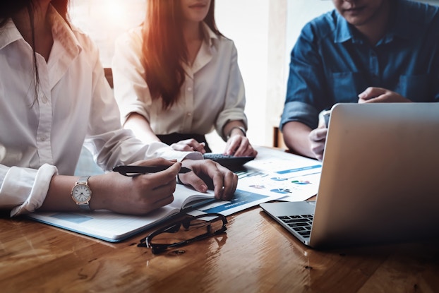 three coworkers in a meeting with laptop and paperwork