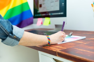  Person working in an office with a rainbow flag and wearing a rainbow bracelet. 