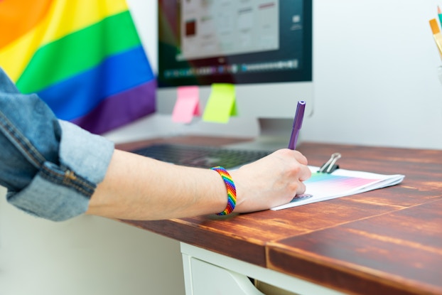  Person working in an office with a rainbow flag and wearing a rainbow bracelet.