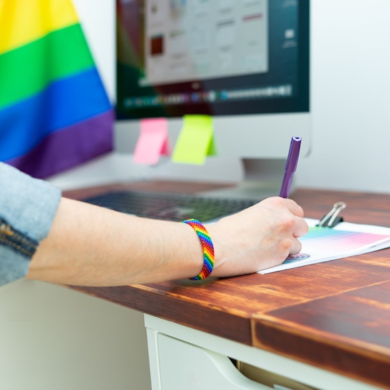 Person working in an office with a rainbow flag and wearing a rainbow bracelet.
