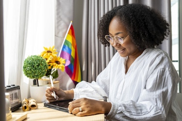  Person working at a desk with a pride flag in the background. 