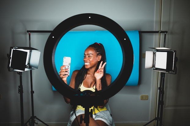 Influencer sitting in front of ring light and taking video on her phone.