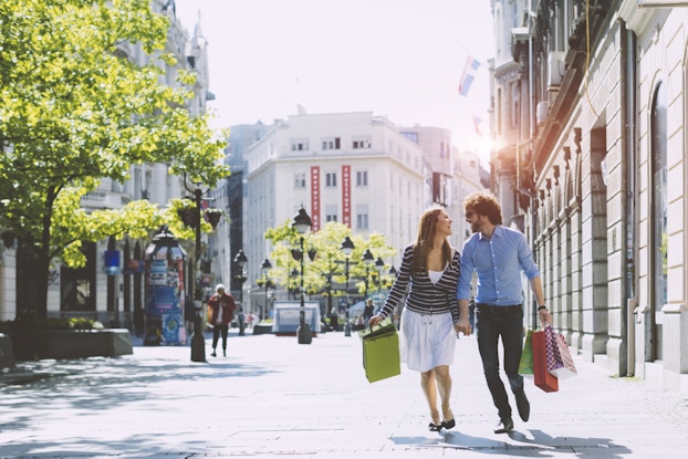 Couple walking down a bright city street holding shopping bags.