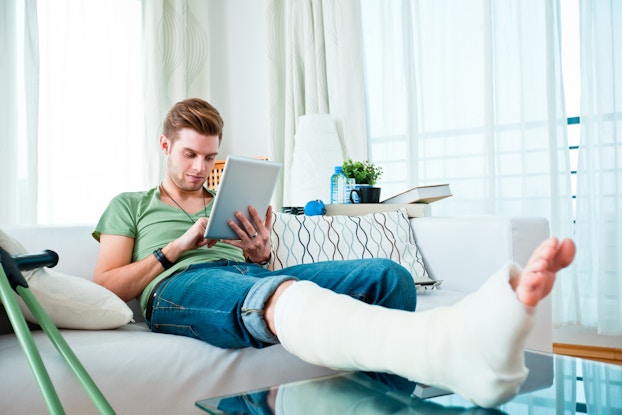  Person sitting at home on the couch with his leg elevated in a cast.