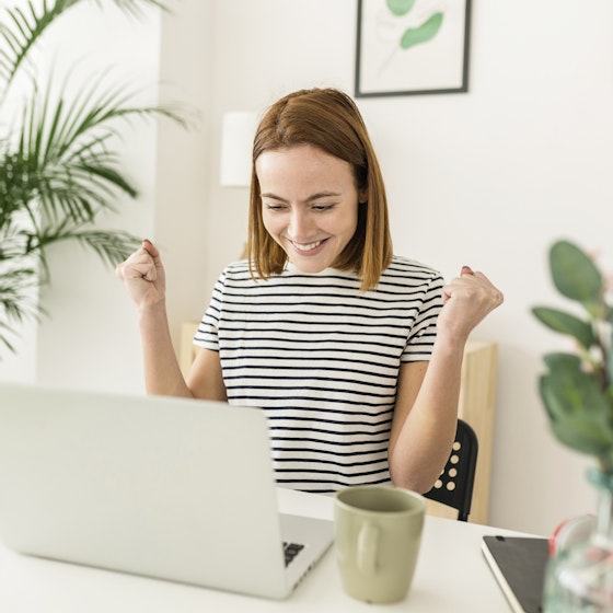 Woman working from home on her laptop, excited with her hands in the air.