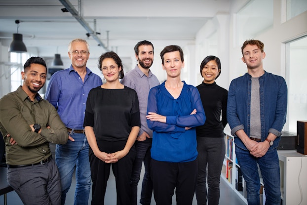 A full shot of a diverse group of seven men and women smiling confidently.