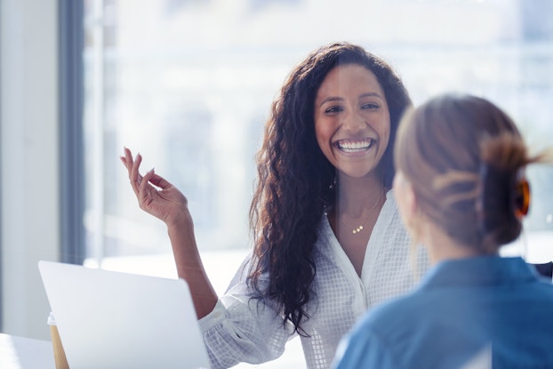 Two coworkers in an office meeting smiling.