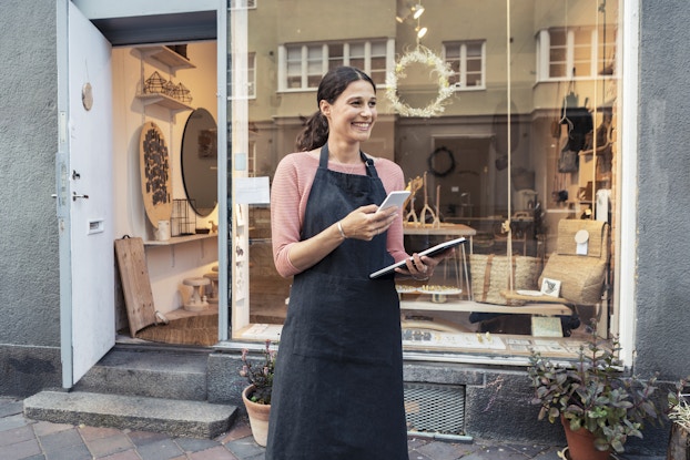 Small business owner outside her shop on her tablet and phone.