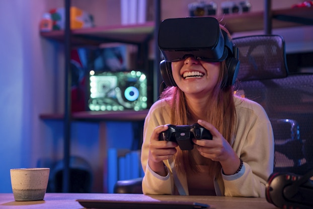  Smiling woman wearing a VR headset and holding a game controller.
