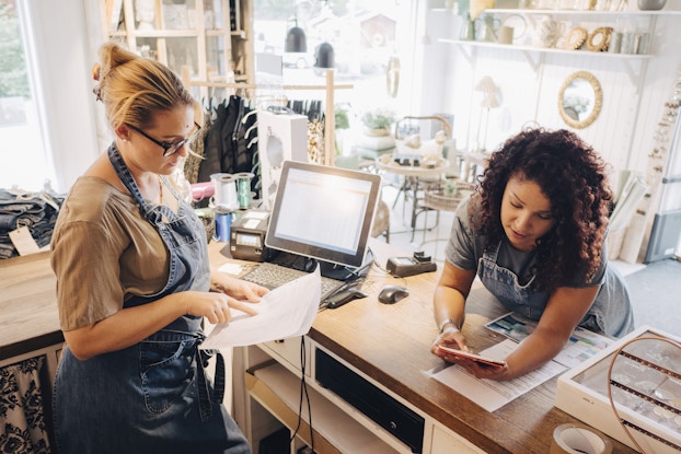  Two colleagues going over receipts a the front desk of their retail business.