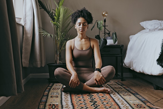 Woman meditating on the floor in her bedroom.