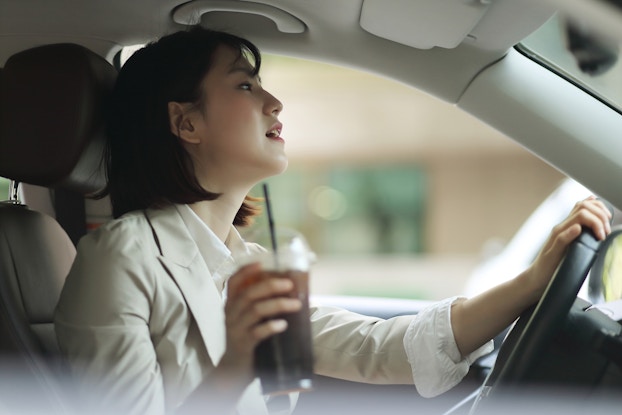  Woman sipping an iced coffee while driving.