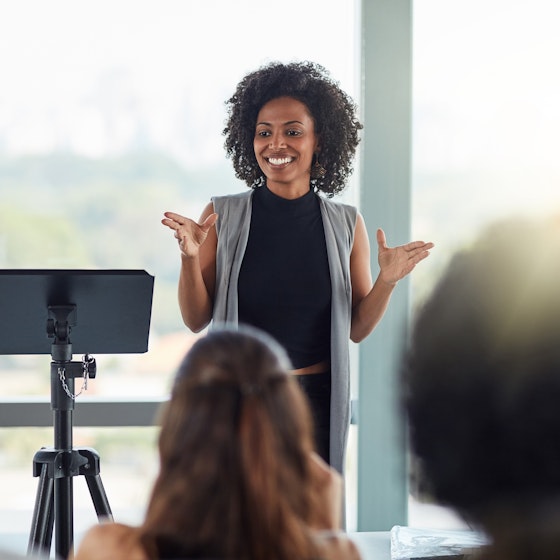 Woman standing in front of a room pitching to a group of people.