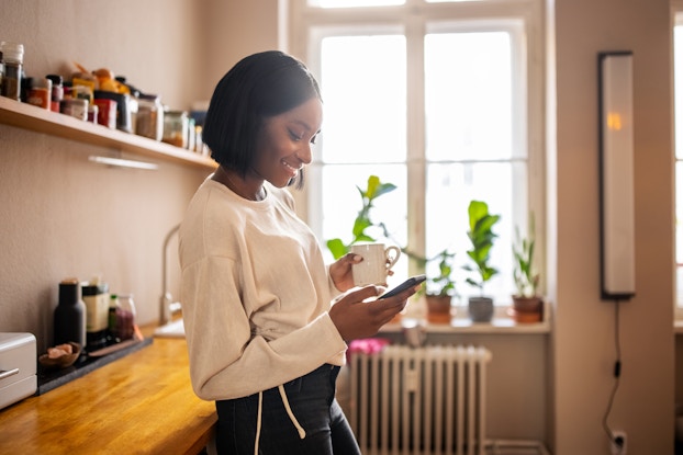  Woman on her phone while drinking coffee inside her apartment.