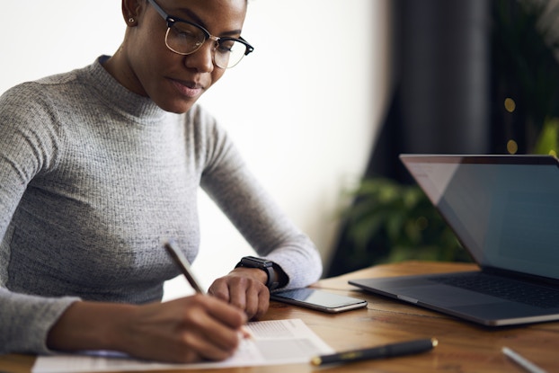 Woman working intently at desk, writing on a pad with a pen.