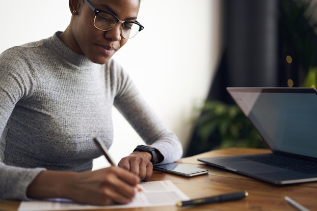  Woman working intently at desk, writing on a pad with a pen.