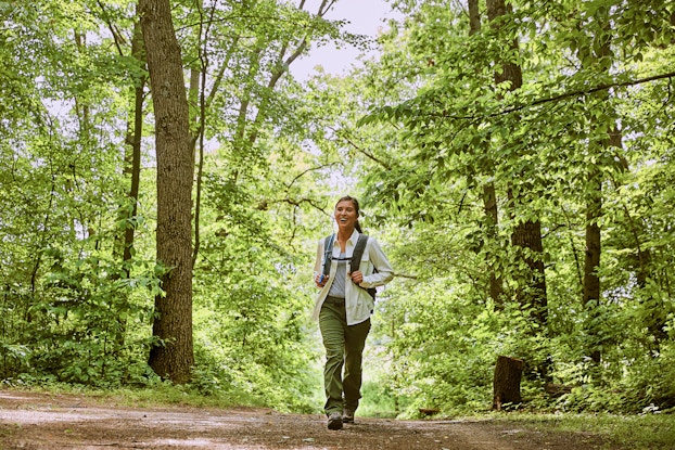  A woman wearing a backpack walks on a trail through a forest.