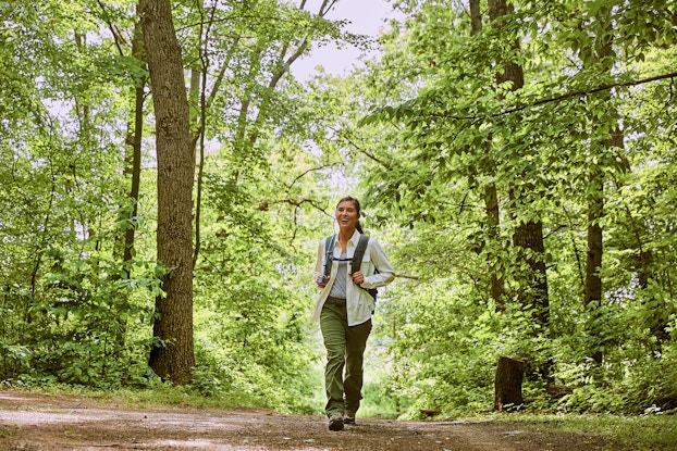 A woman wearing a backpack walks on a trail through a forest.