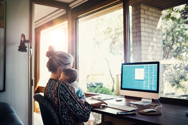  woman holding baby while working at home on laptop