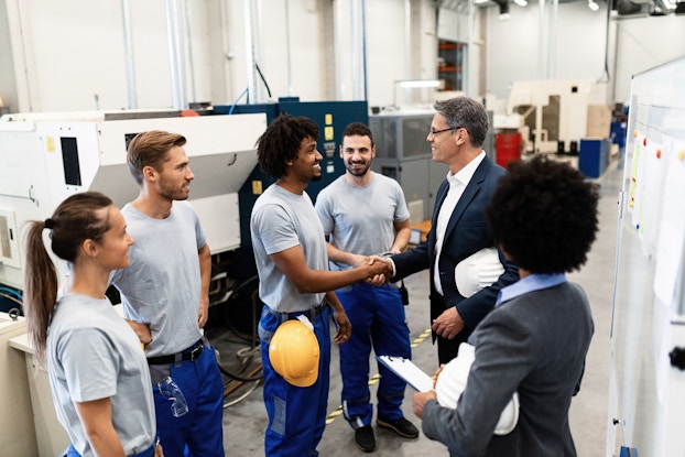  Company manager shakes an employees' hand on the assembly line floor.