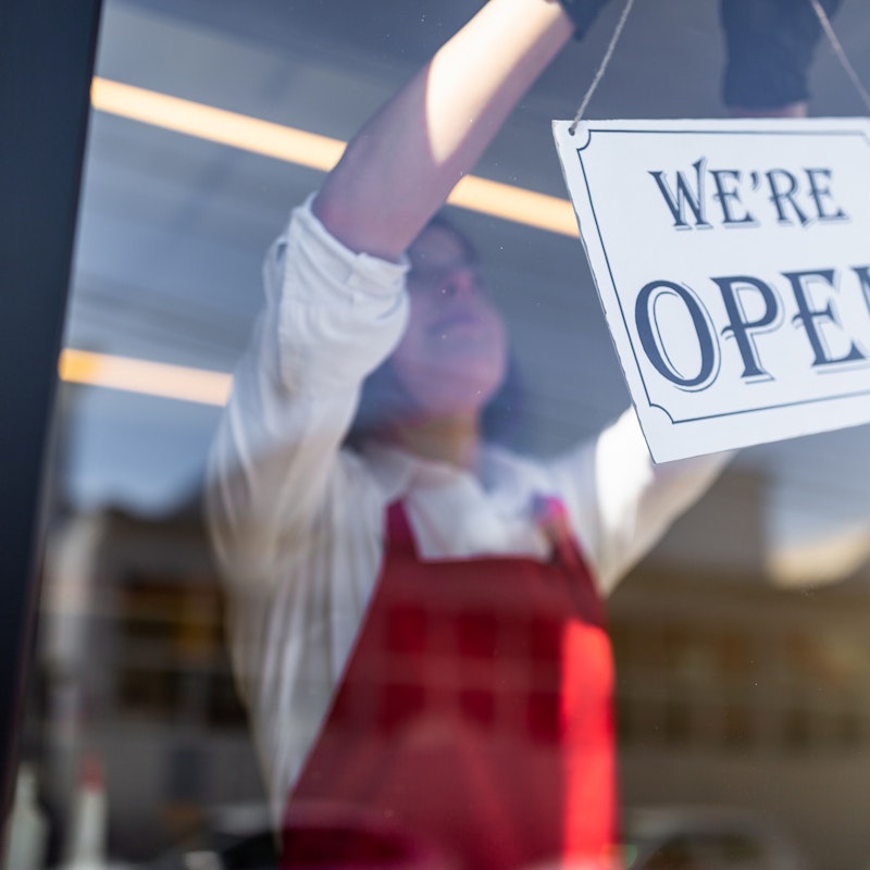 Business owner wearing a red apron and hanging a "we're open" sign in the business window.