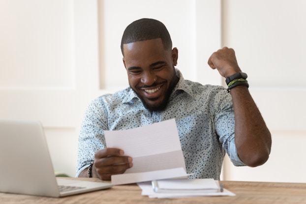 A man smiles and pumps his fist in response to something he reads on a piece of paper.