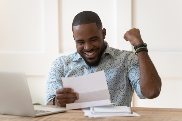  A man smiles and pumps his fist in response to something he reads on a piece of paper.