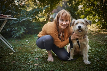 A woman is pictured with her dog in her garden. Both the woman and the dog are looking directly at the camera.