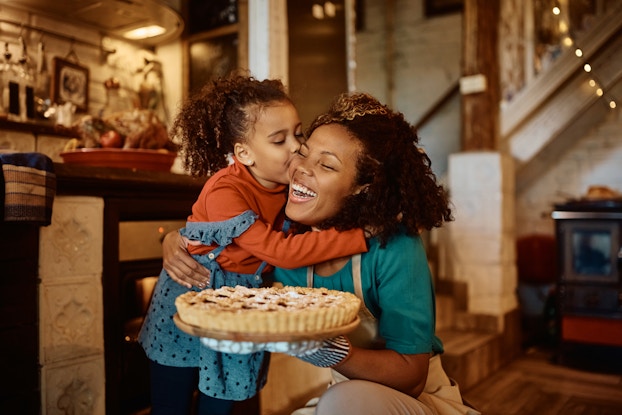  Smiling mother and daughter holding a freshly baked pie inside their kitchen.