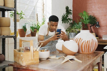  A young man taking pictures of his finished vases with a smartphone in a pottery studio. 