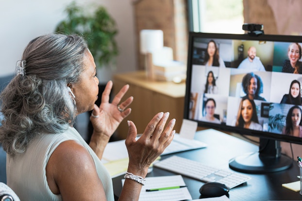  Woman presenting from her home office to a computer screen full of virtual attendees.