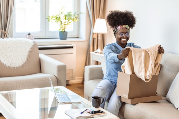  Happy woman inside her home opening a package and pulling out a sweater.
