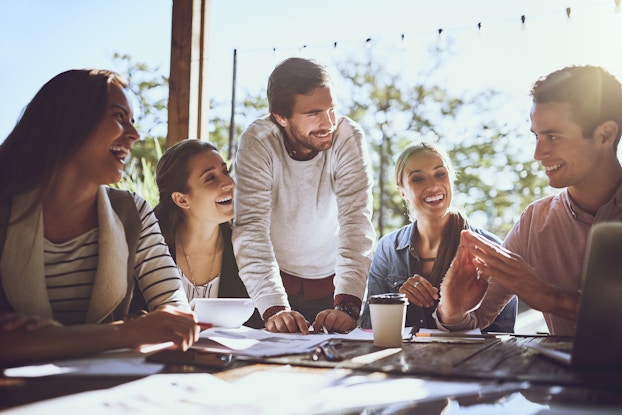 Group of coworkers huddled at a table smiling and laughing.